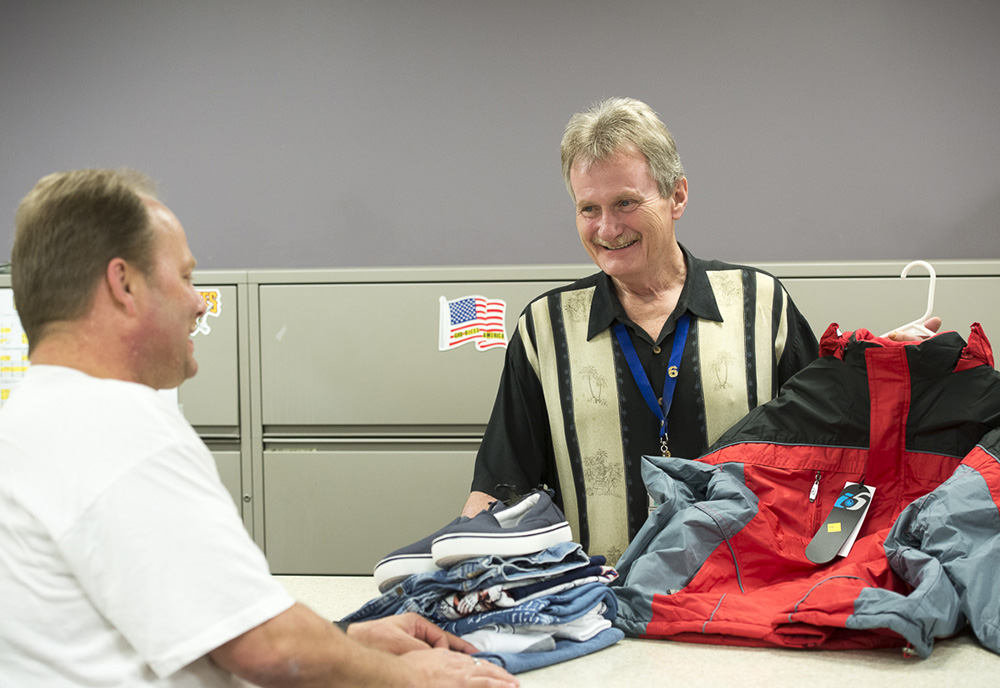 Image of a male volunteer handing out clothes to a male Veteran. 